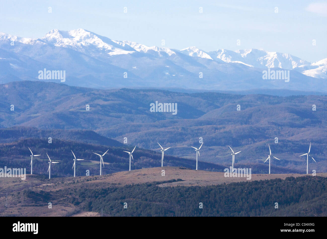 Fila di dieci wind-turbine sulle colline in anticipo delle montagne coperte di neve dei Pirenei, fattoria del vento nel sud della Francia Foto Stock