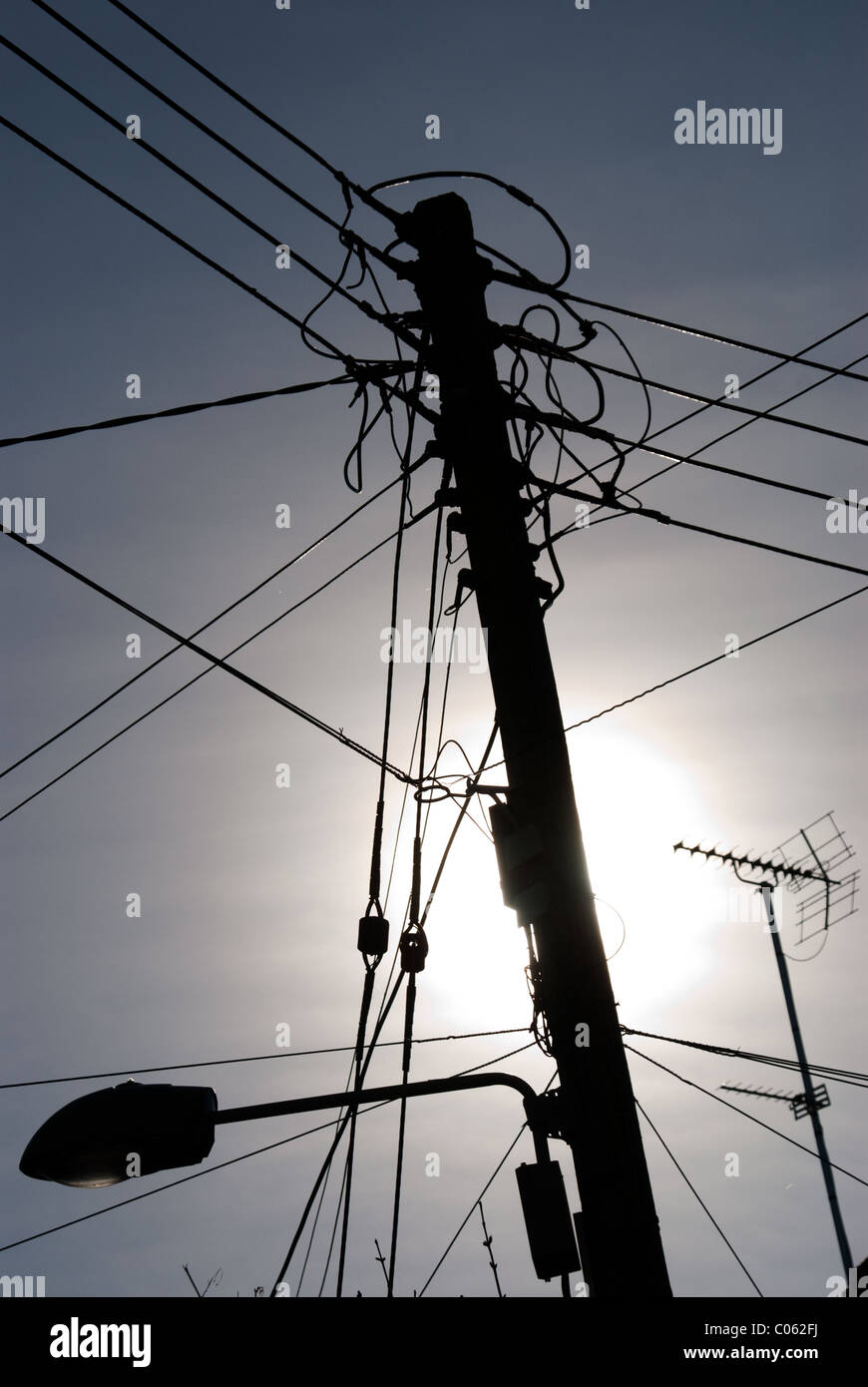 Un "telegrafo polo' con molte utilità di overhead di cavi di alimentazione o i fili su di essa, contro un cielo chiaro. Il sole è dietro la pole. Foto Stock