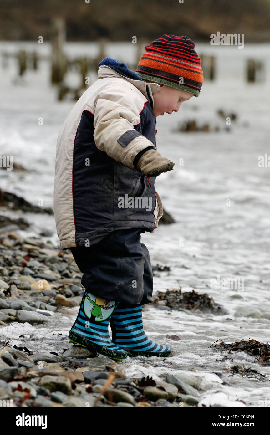 Un giovane ragazzo giocando sulla spiaggia in una fredda giornata. Foto Stock