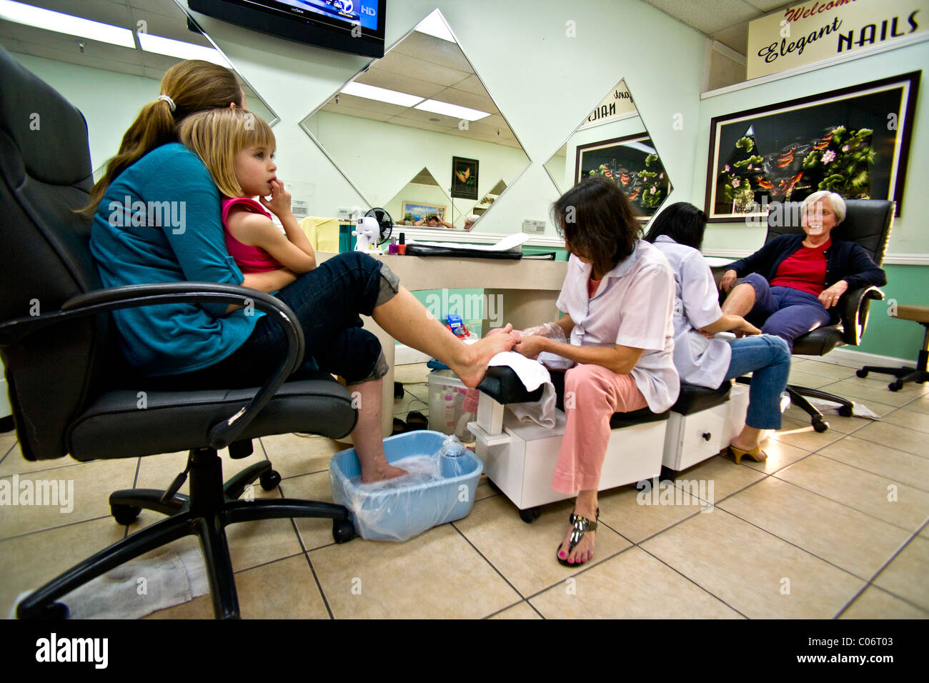 Una donna vietnamita tecnico effettua una pedicure per una donna che tiene la sua giovane figlia in un Southern California salon. Foto Stock