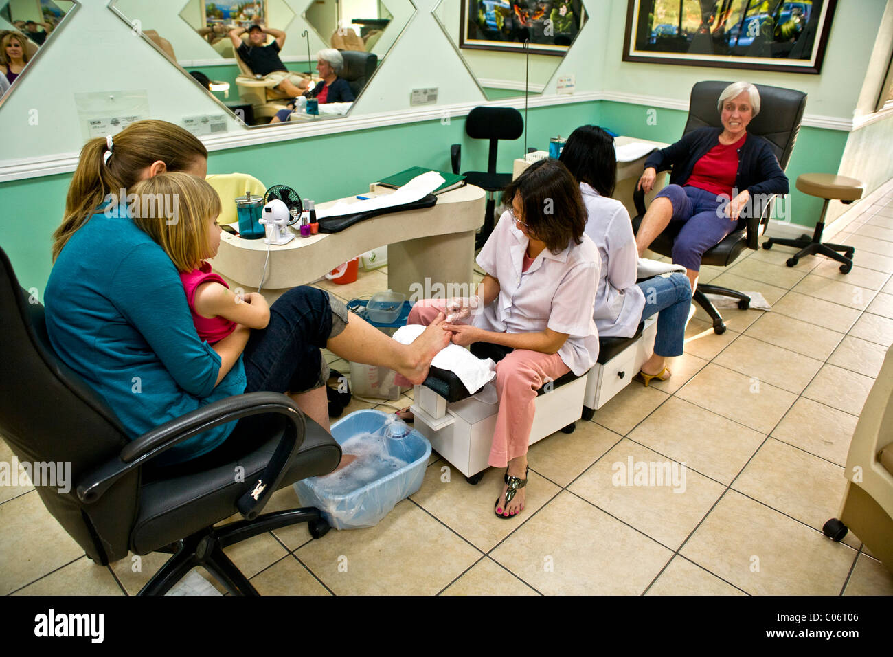 Una donna vietnamita tecnico effettua una pedicure per una donna che tiene la sua giovane figlia in un Southern California salon. Foto Stock