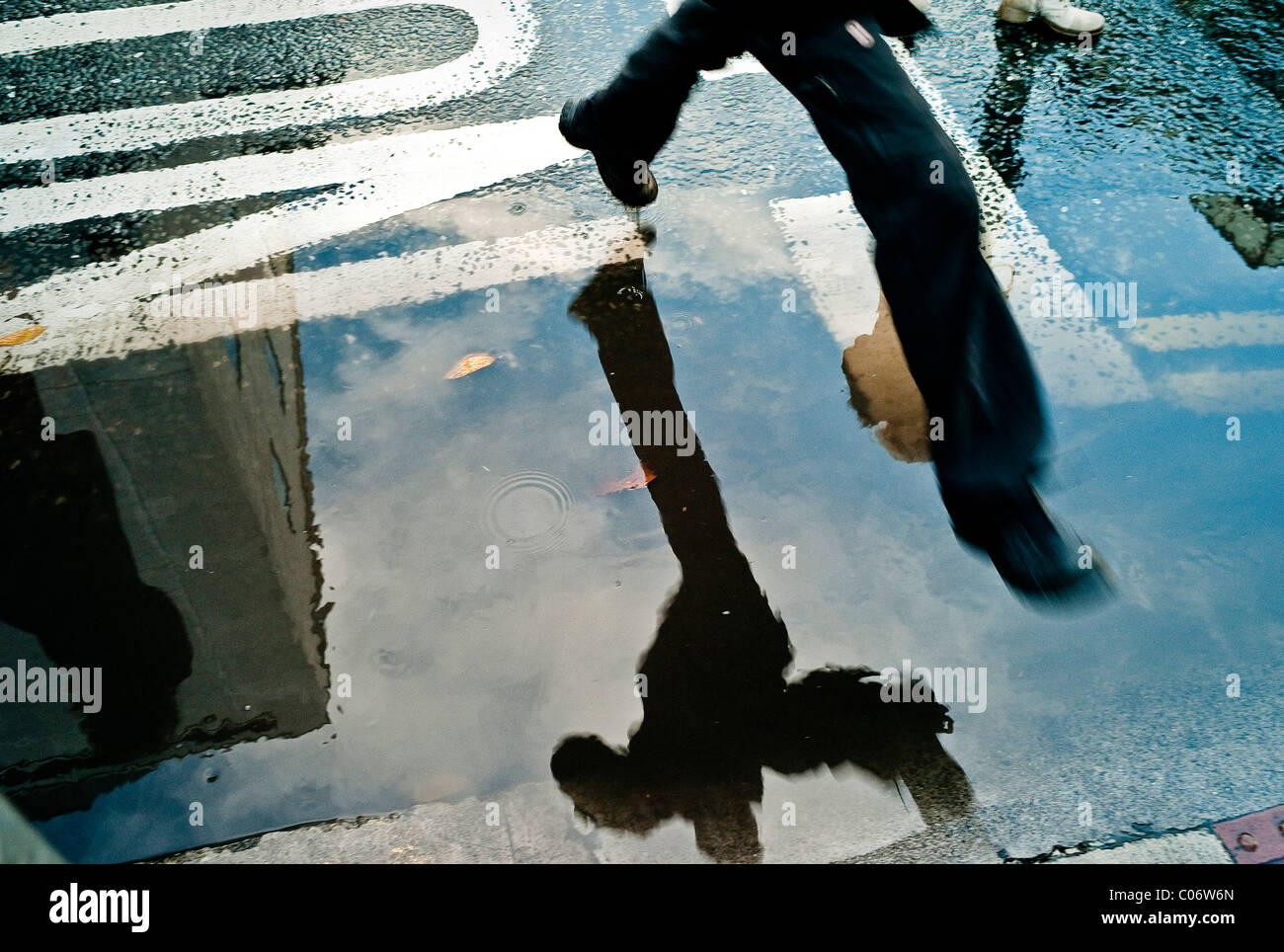 Un uomo salta su una pozza di acqua sul lato della strada. Foto Stock