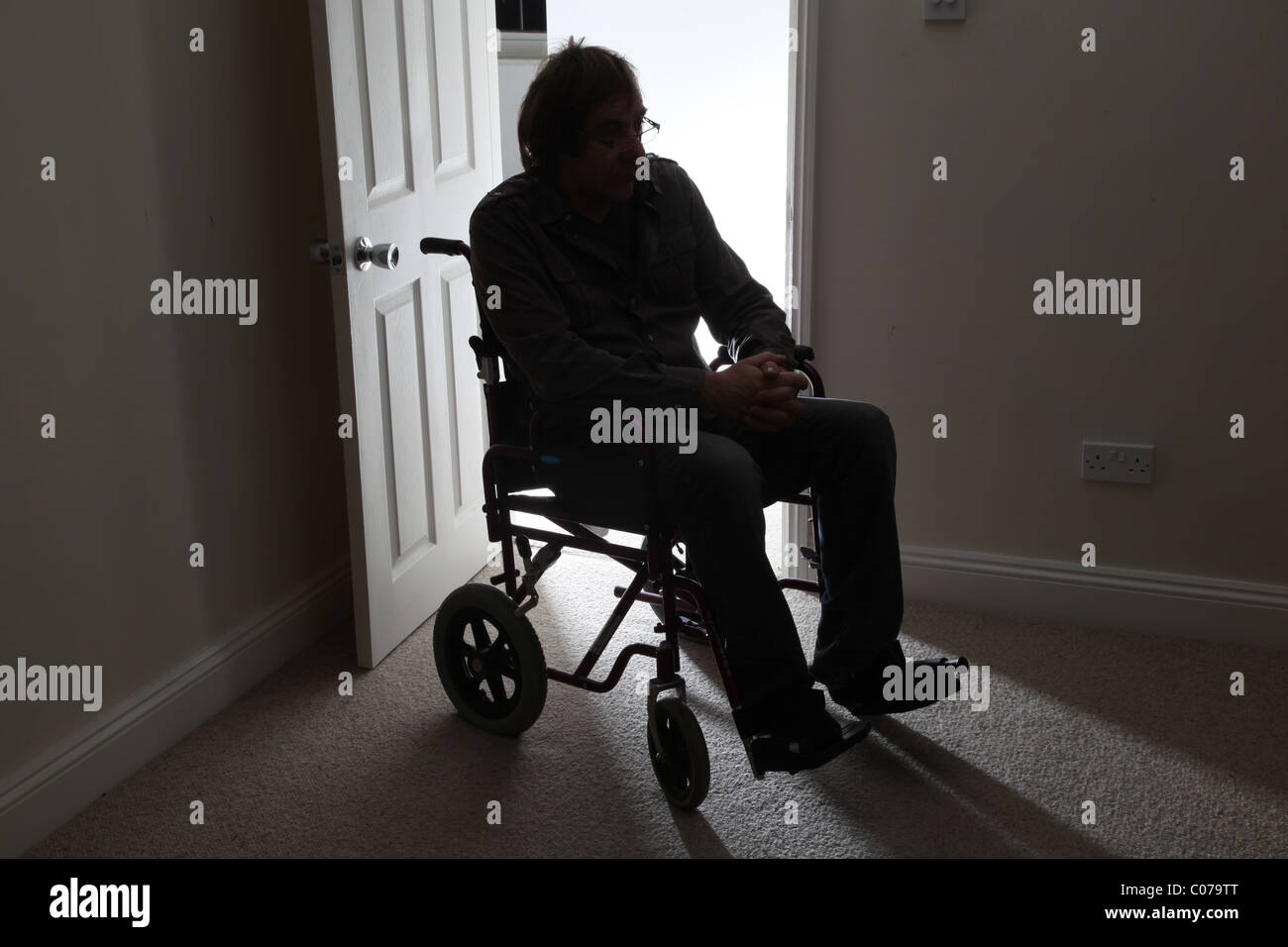 Uomo in sedia a rotelle, seduto da solo in una stanza buia. Foto Stock