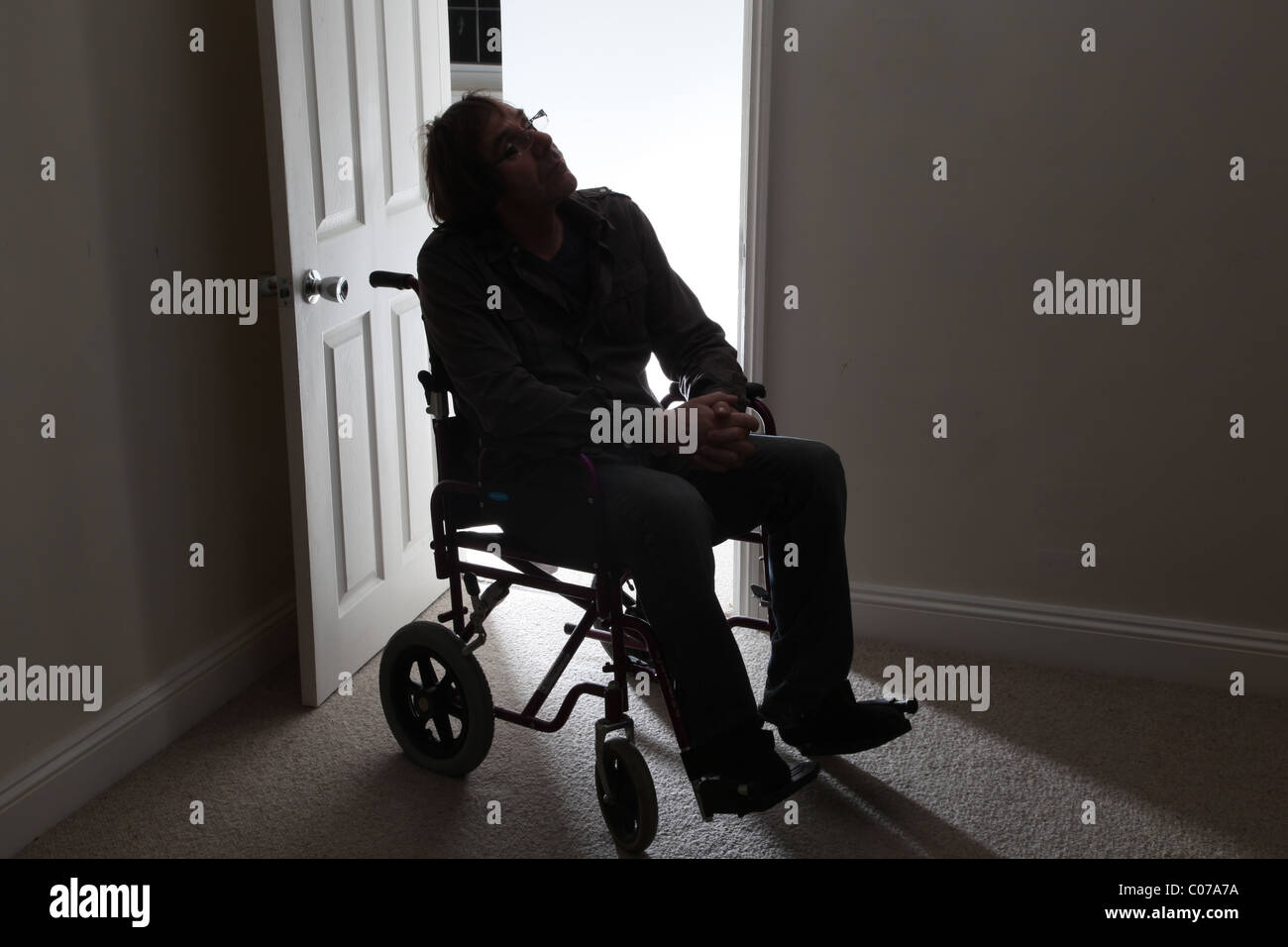 Uomo in una sedia a rotelle da solo da una porta aperta Foto Stock