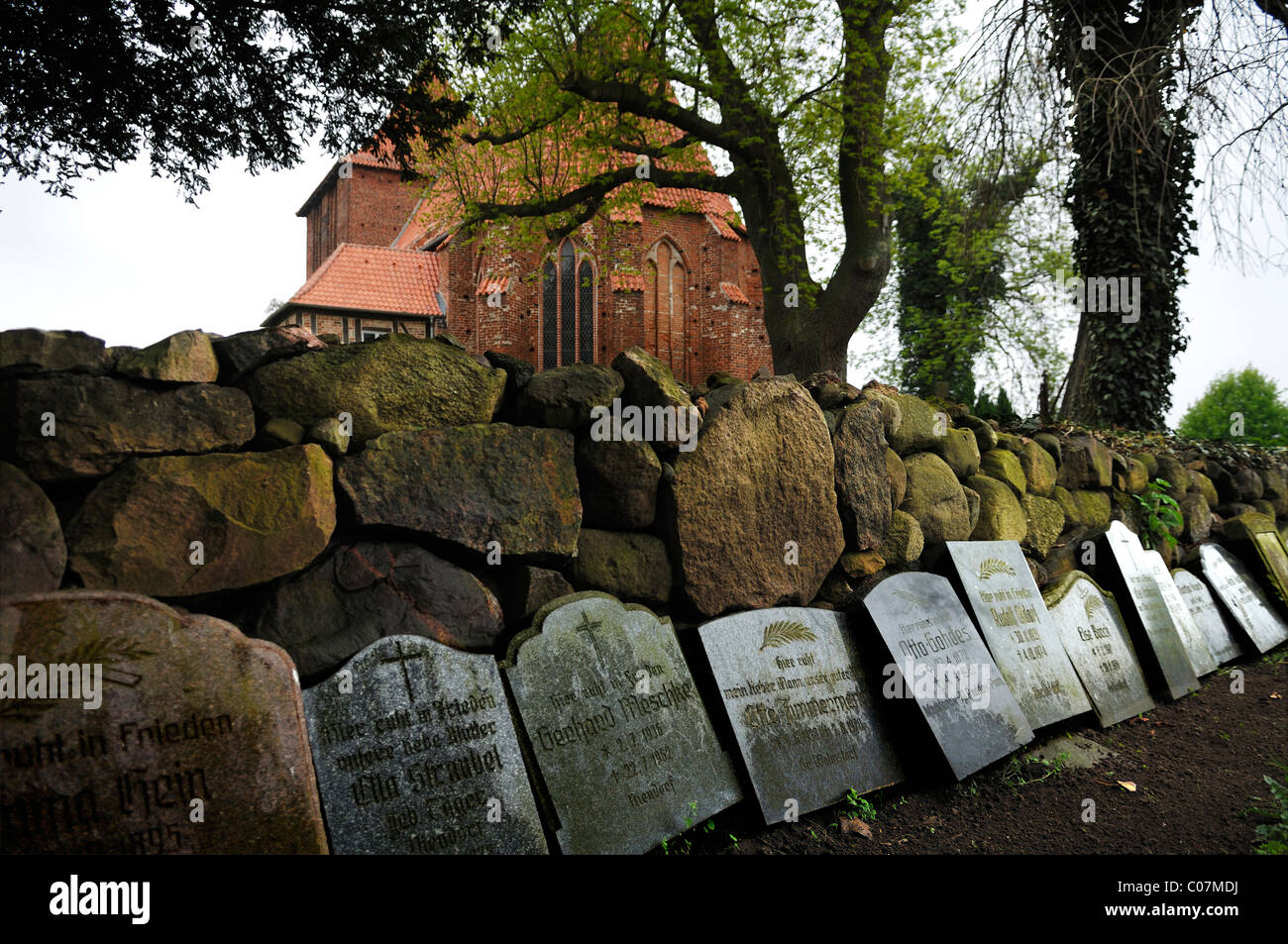 Tomba di lastre appoggiata contro un muro a secco fatti di blocchi irregolari, nel vecchio cimitero del villaggio, antico villaggio chiesa dal XV Foto Stock