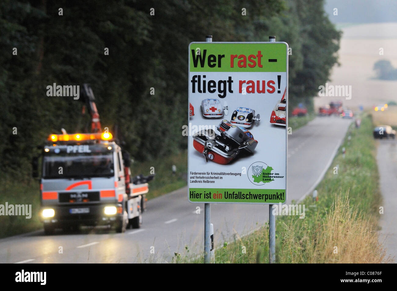 Segno di traffico attenzione a guidare in modo sensato sul B 39 road, con un passaggio di trainare camion che trasportano il relitto di un automobile in cui tre Foto Stock