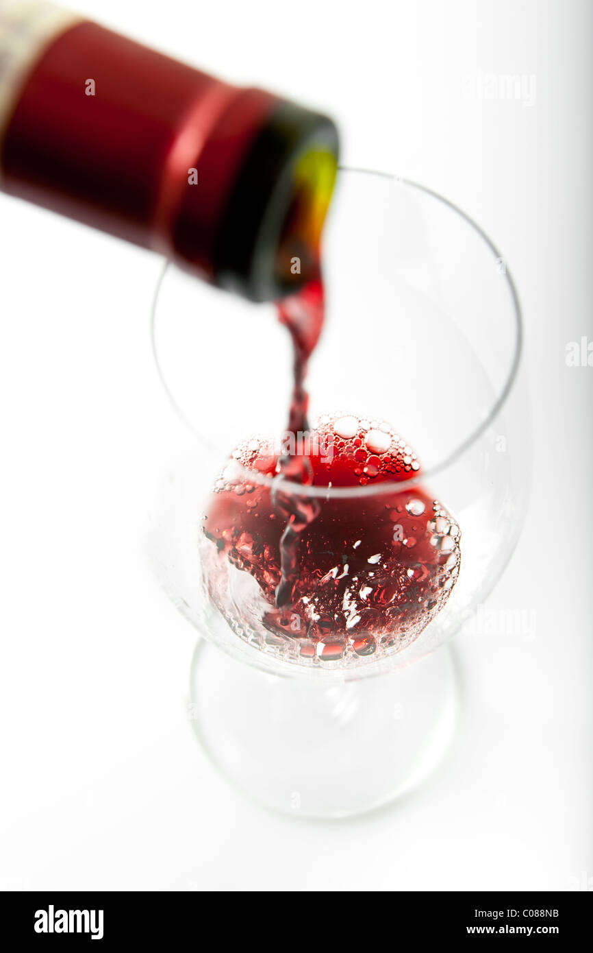 Un bicchiere di vino rosso che viene versato di bottiglia su uno sfondo bianco. Foto Stock