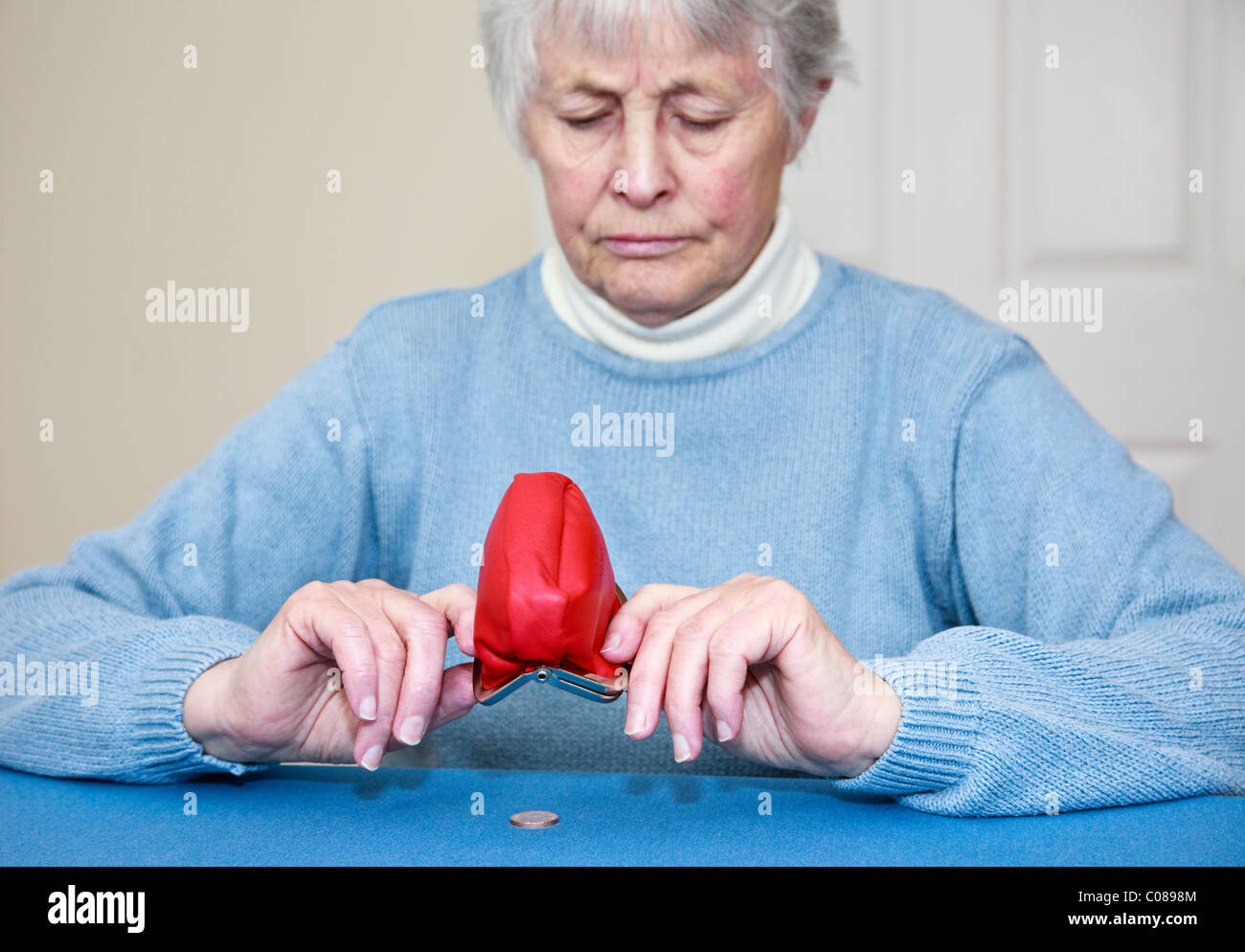 Senior povera donna anziana pensionata con nessun denaro e un'espressione preoccupata lo svuotamento di un centesimo moneta al di fuori di un portamonete aperto in epoca di austerità. Inghilterra, Regno Unito Foto Stock