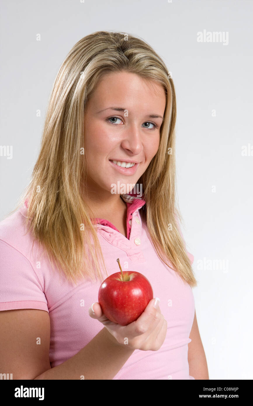 Una giovane donna sorride tenendo una mela rossa Foto Stock