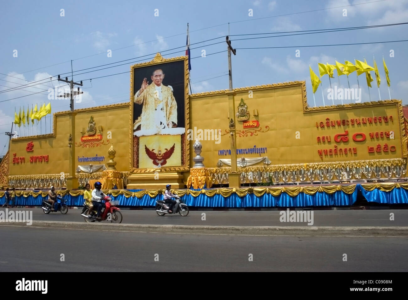 Le persone a guidare moto sono passato di pilotaggio di un display con una fotografia del Re Rama IX su una strada di città in Ayuttaya, Thailandia. Foto Stock