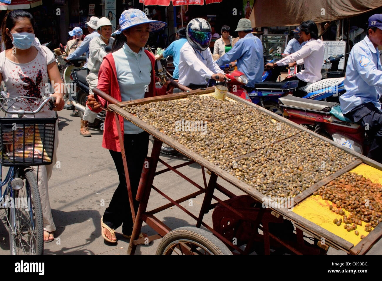 Una donna fornitore di cibo sta spingendo un carrello carico di lumache su una strada trafficata in Phnom Penh Cambogia. Foto Stock