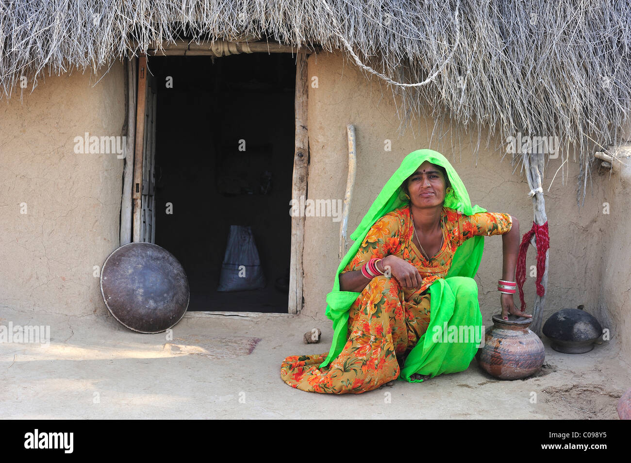 Donna con un contenitore di acqua seduto di fronte a una casa tradizionale deserto di Thar, Rajasthan, India, Asia Foto Stock