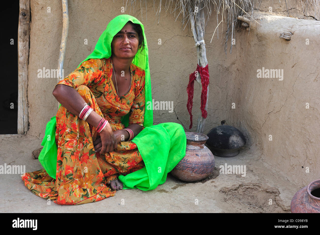 Donna con un contenitore di acqua seduto di fronte a una casa tradizionale deserto di Thar, Rajasthan, India, Asia Foto Stock
