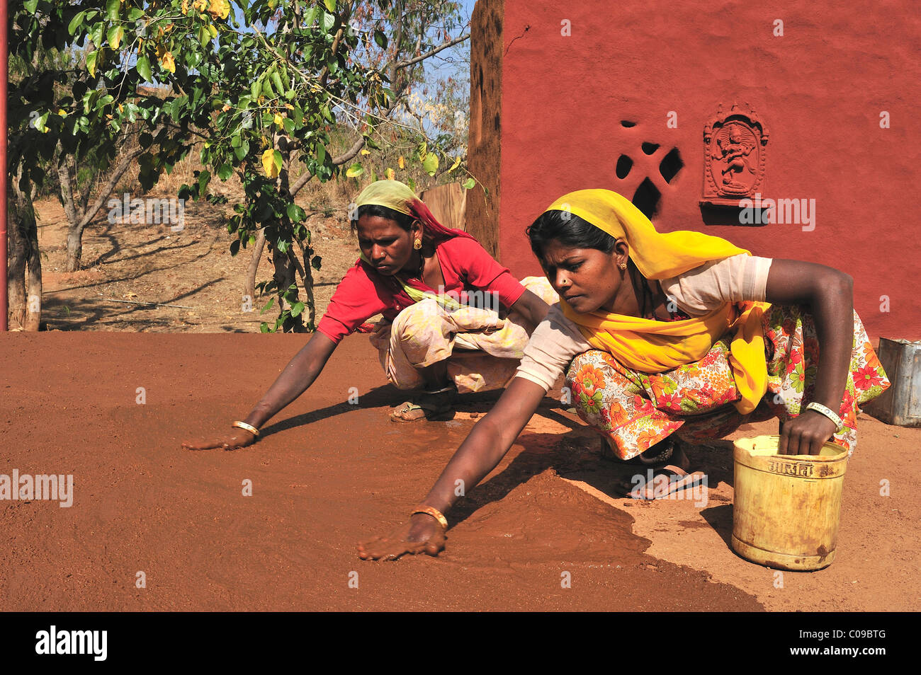 Due donne intonacare il pavimento di un cortile interno con una miscela di sterco di vacca e la sabbia del deserto di Thar, Rajasthan, India, Asia Foto Stock