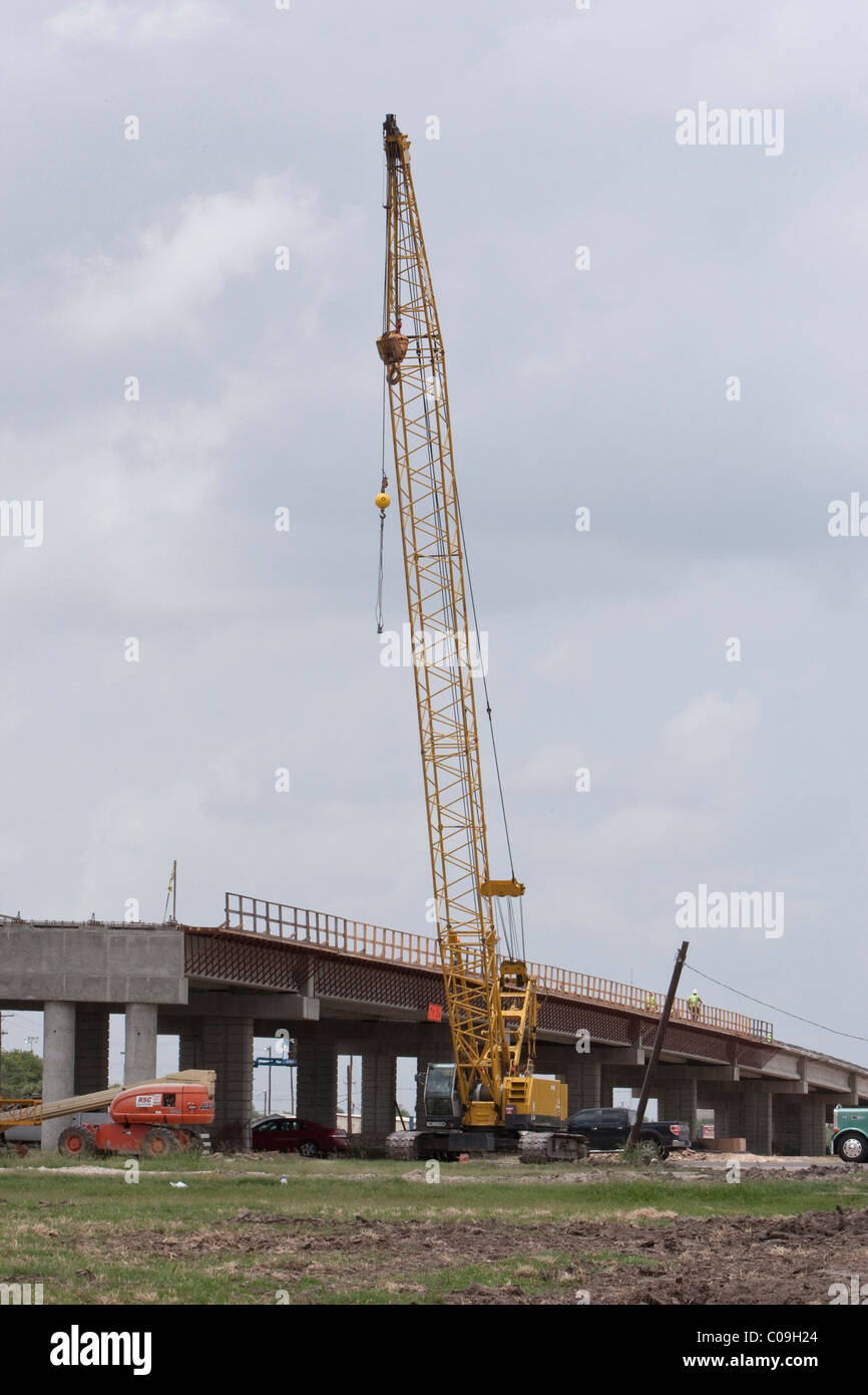 Gru cingolate assiste con travi di sollevamento per la costruzione di ponte sull'autostrada trafficata al sito in costruzione in Raymondville Texas USA Foto Stock