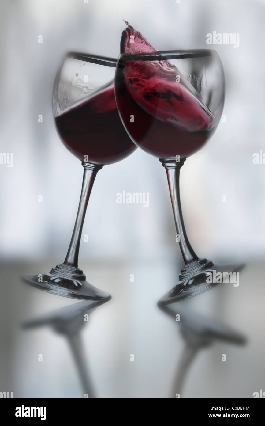 Dancing vino rosso bicchieri inclinato in un brindisi per ogni altro con movimento dinamico, vino debordi, stelo curvo di vetro Foto Stock