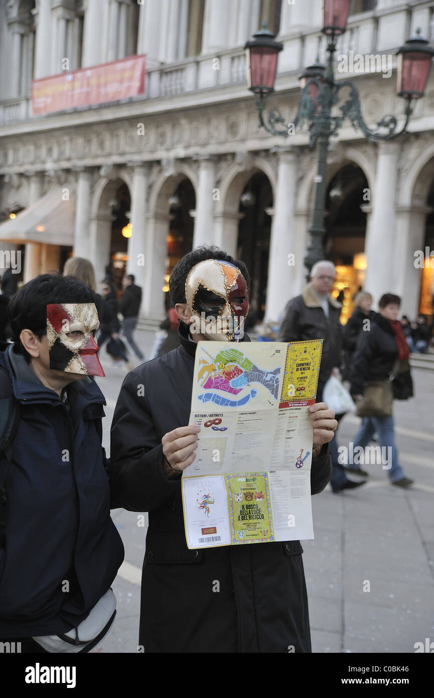 Tourist indossando maschere veneziane controllare il programma del Carnevale 2011 in San Marco Foto Stock