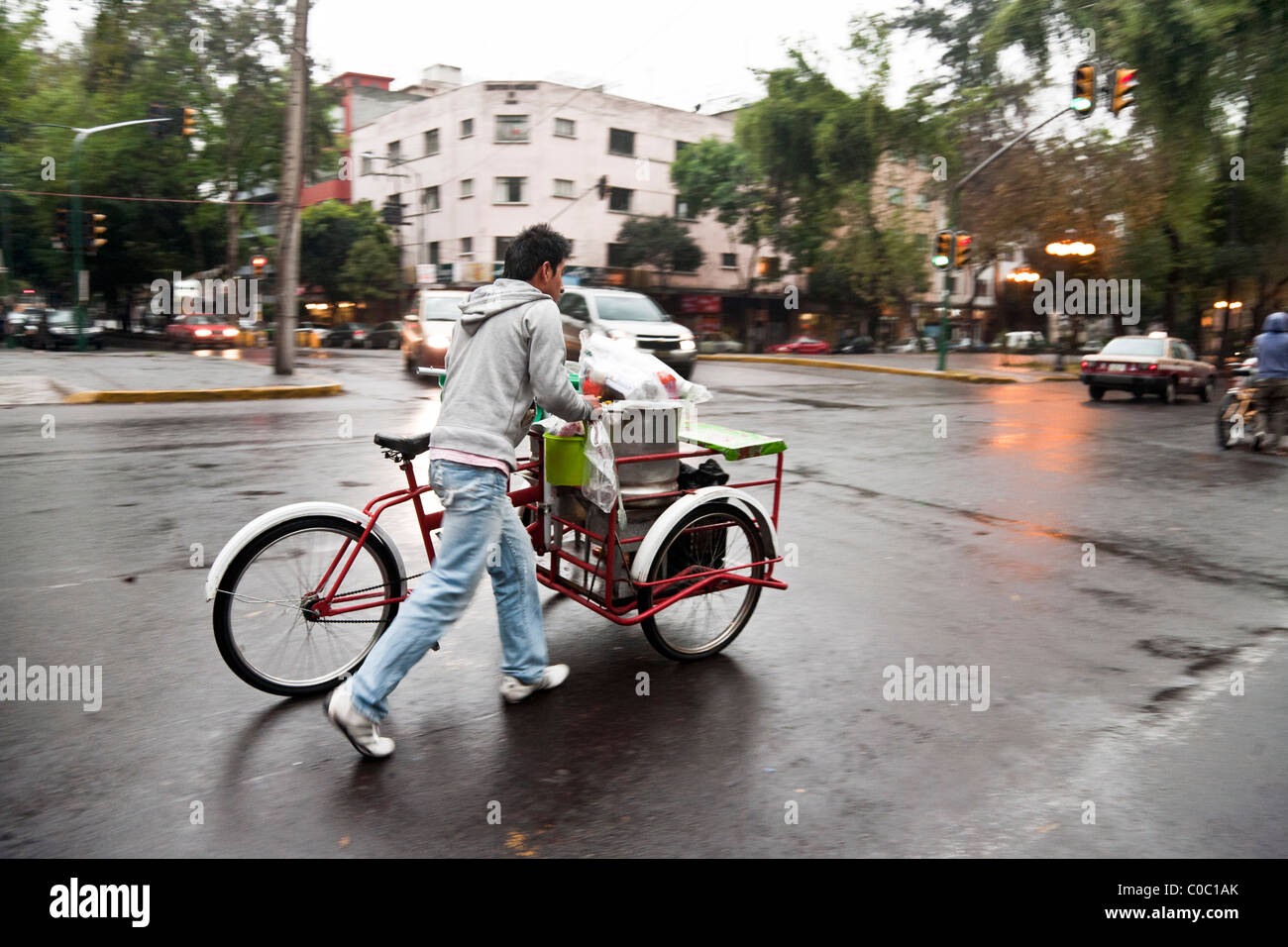 Giovane messicano fornitore modificato di spinta 3 ruota carrello bicicletta lungo Avenida Alvaro Obregon su bagnato serata fredda nel quartiere di Roma Foto Stock