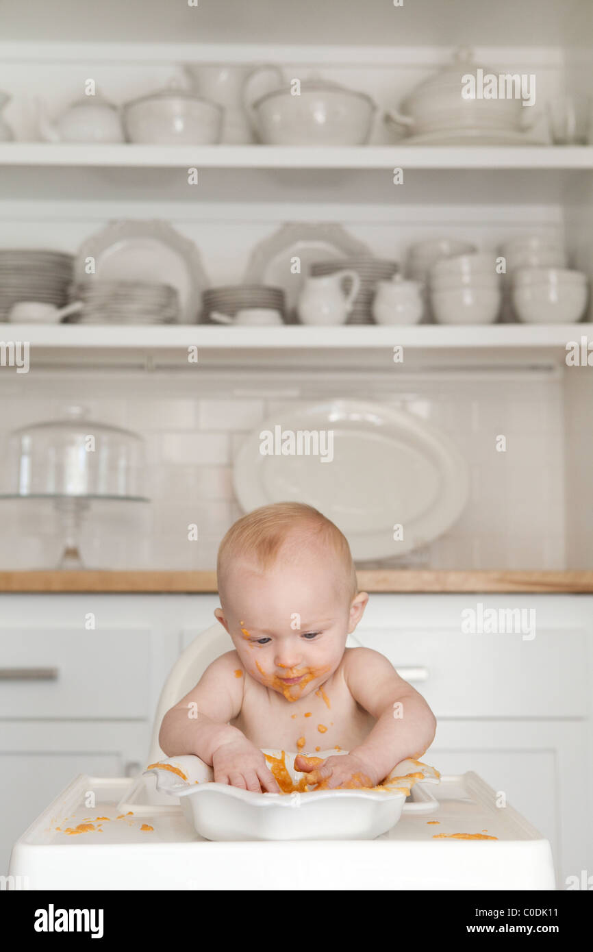 Confuso baby eating in sedia alta Foto Stock