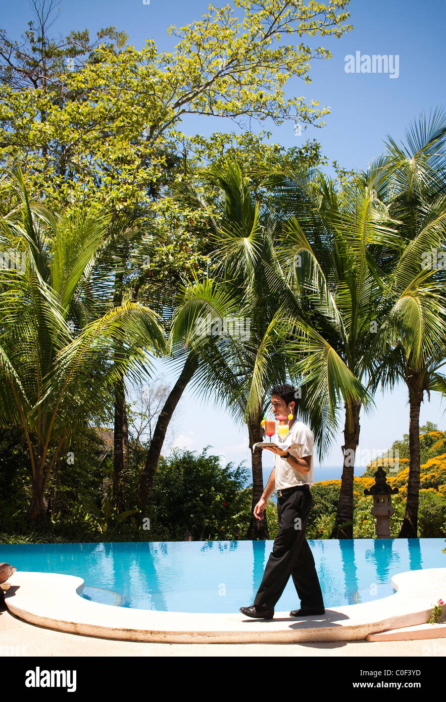Un cameriere passeggiate passato una piscina esterna in una giornata di sole per offrire due bevande. Foto Stock