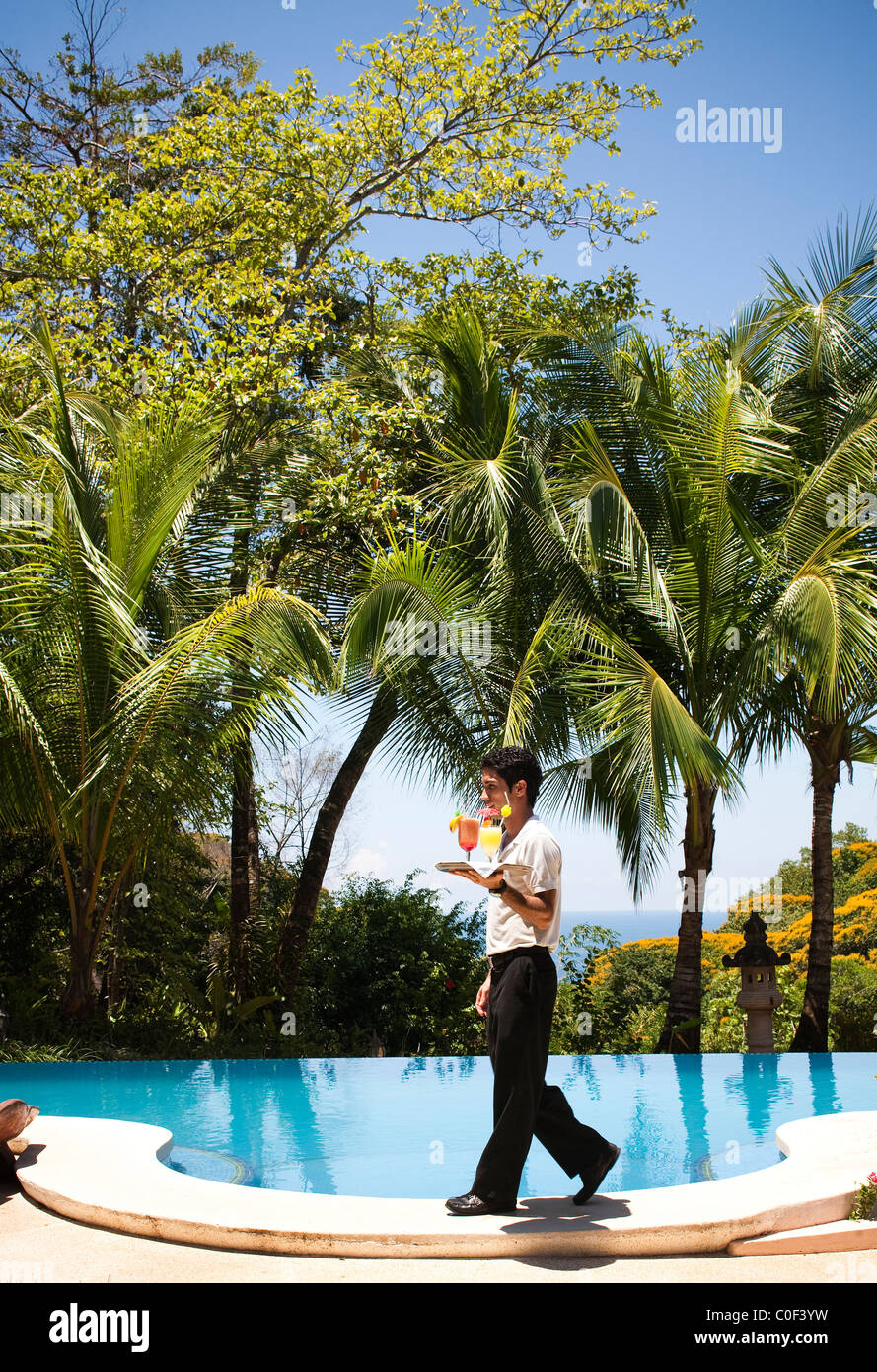 Un cameriere passeggiate passato una piscina esterna in una giornata di sole per offrire due bevande. Foto Stock