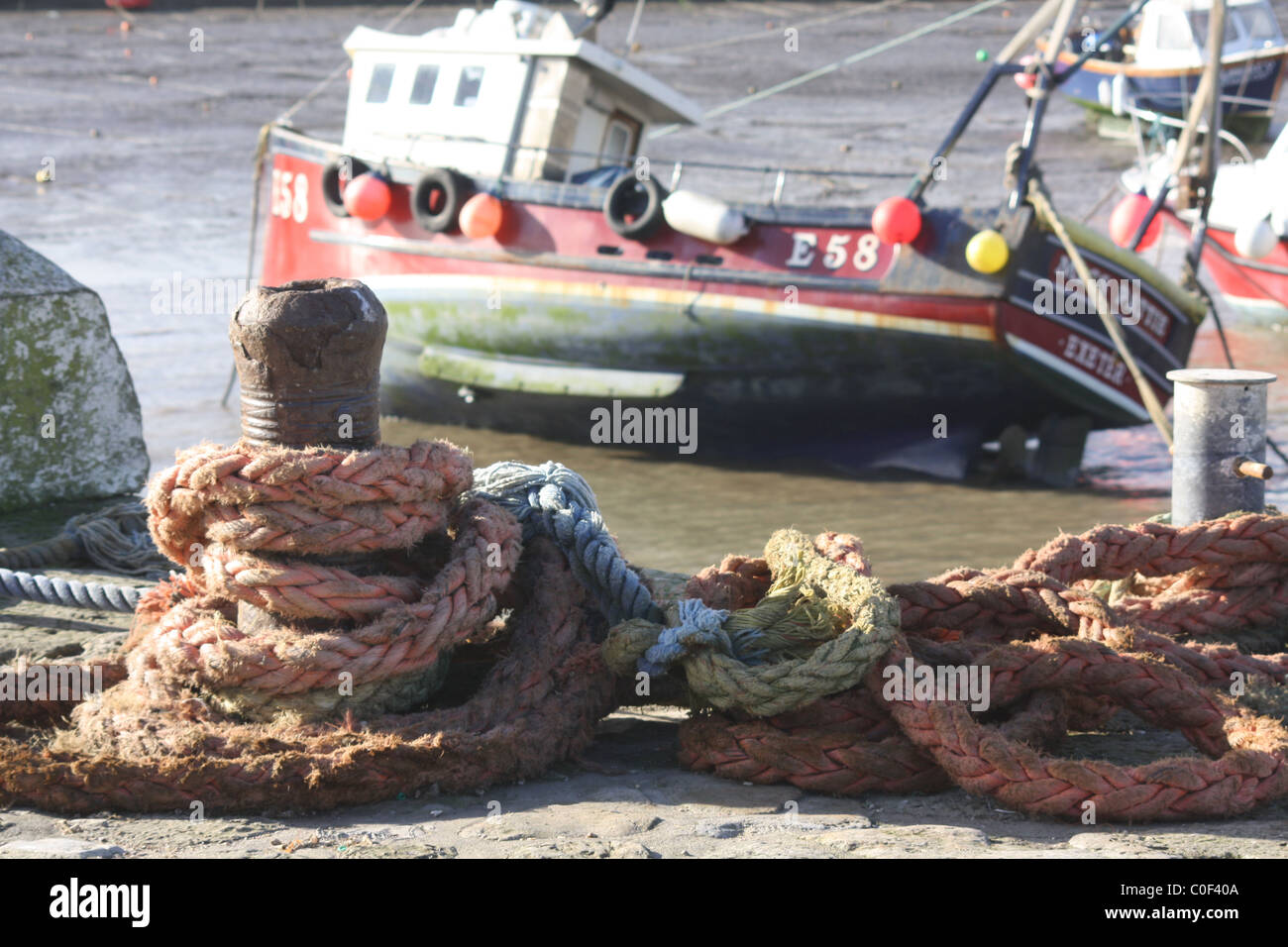 Corde per impieghi pesanti legate al bullard a Lyme Regis in primo piano con una barca da pesca in parte a terra su sabbia morbida a bassa marea sullo sfondo. Foto Stock