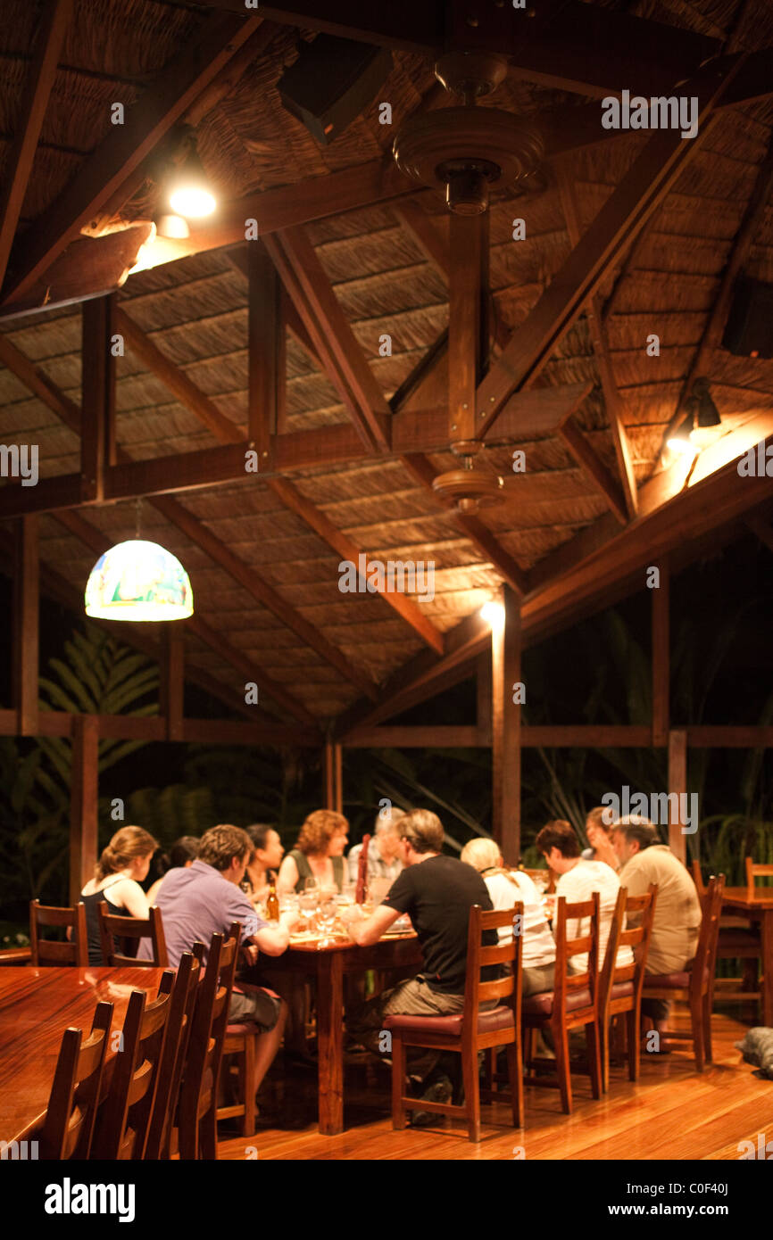 Un gruppo di persone in vacanza a mangiare in una tavola al di sotto di una struttura di legno in un ecolodge in un paese straniero. Foto Stock