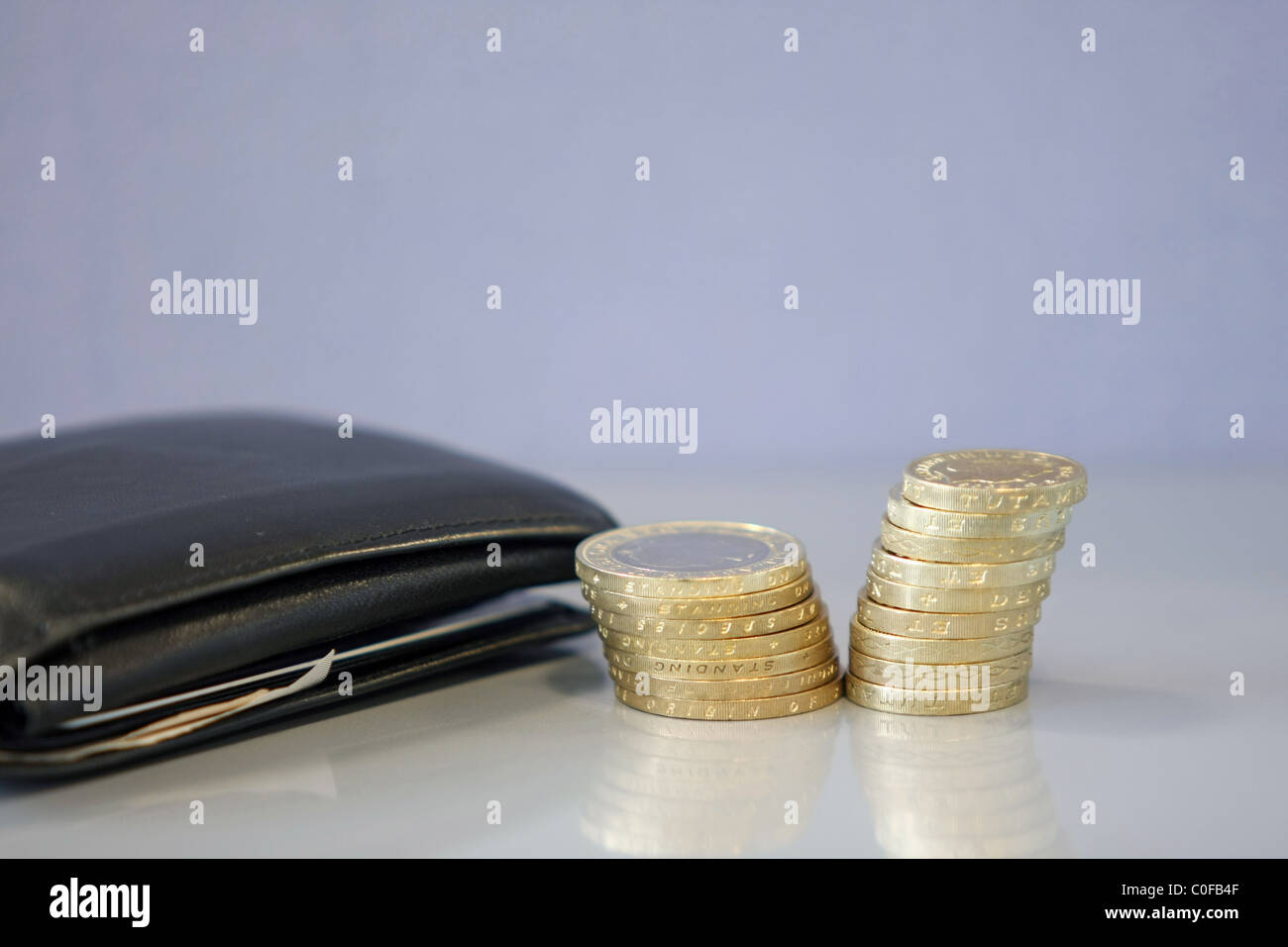 Pile di sterling £2 e £1 monete accanto a un portafoglio nero Foto Stock
