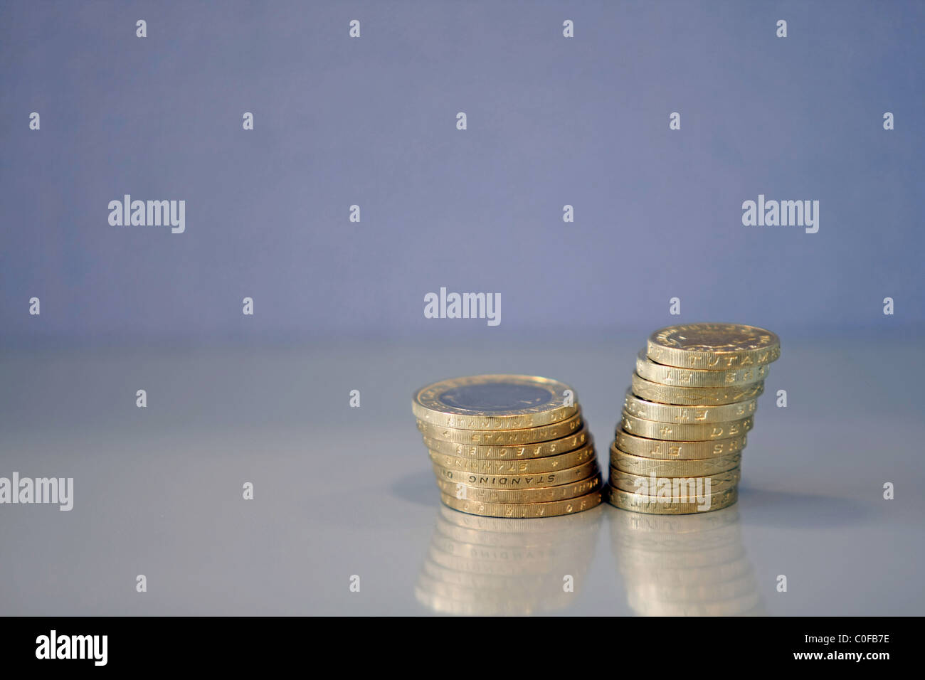Una pila di sterling £2 monete accanto a una pila di £ 1 monete contro uno sfondo blu Foto Stock