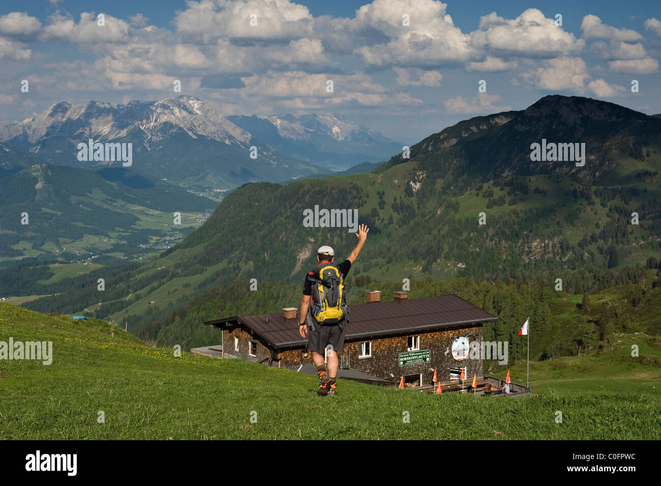 Un maschio di escursionista onde ai suoi compagni hikers seduto in una baita di montagna a Kitzbuheler Horn Kitzbuehel Tirolo, Austria Foto Stock