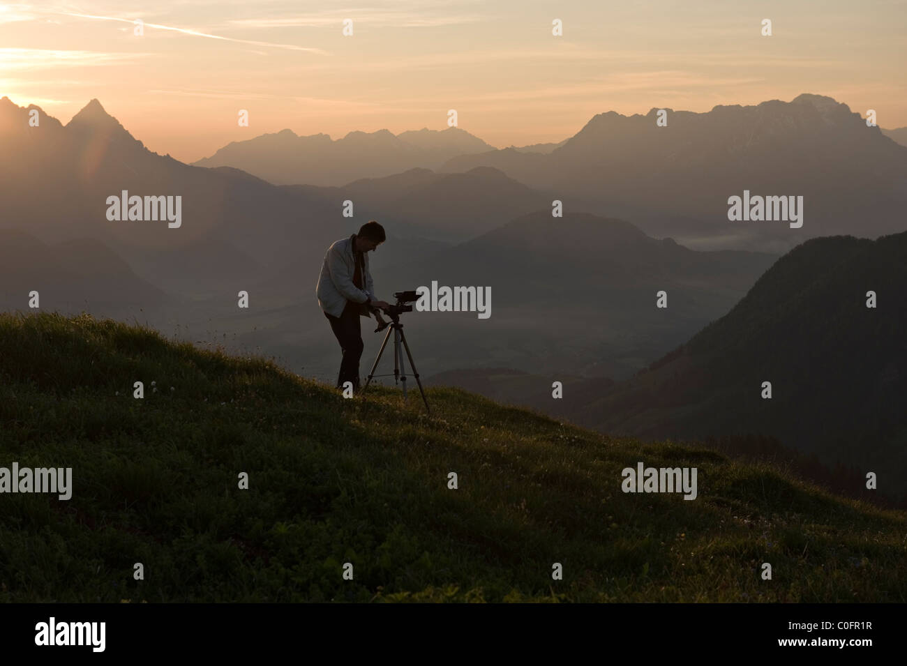 Un uomo imposta la sua telecamera all'alba Kitzbuheler Horn Kitzbuhel Tirolo, Austria Europa Foto Stock