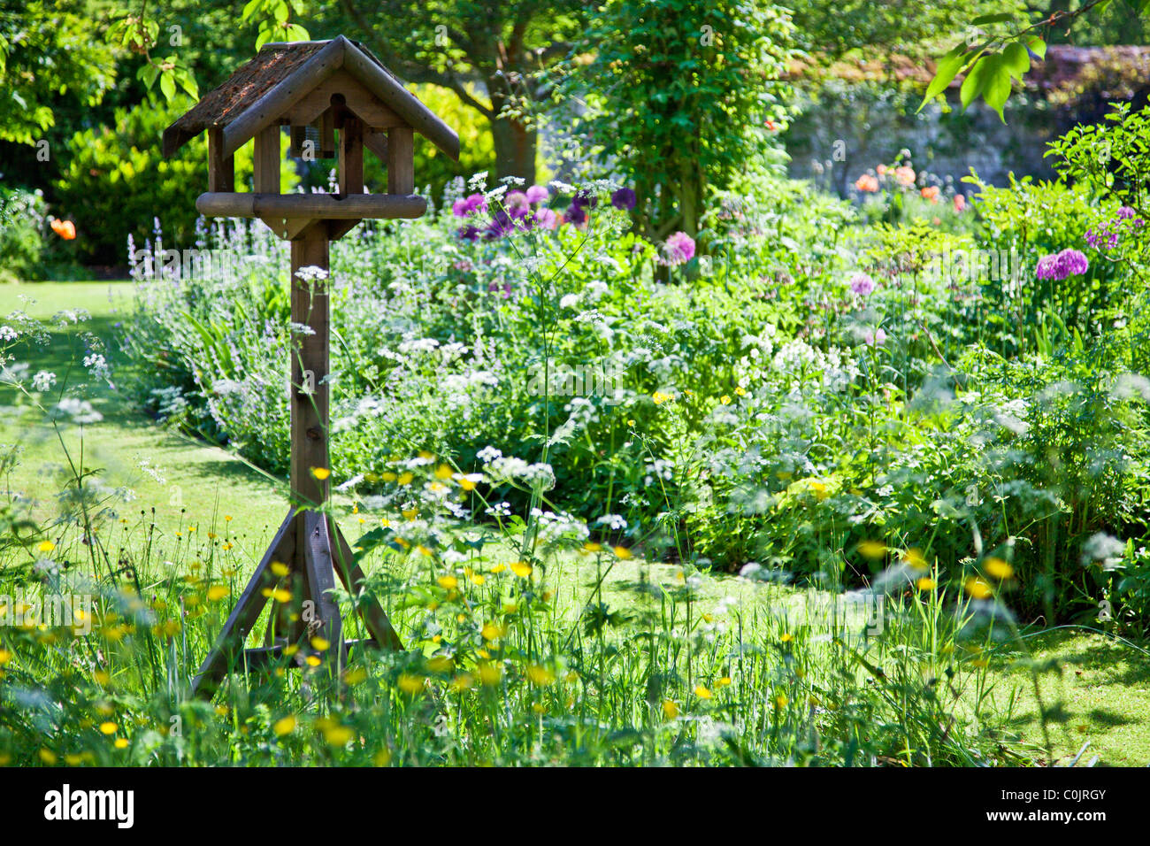 Un grazioso, rustico legno bird tabella impostata tra aiuole o letti in un paese di lingua inglese giardino in estate Foto Stock
