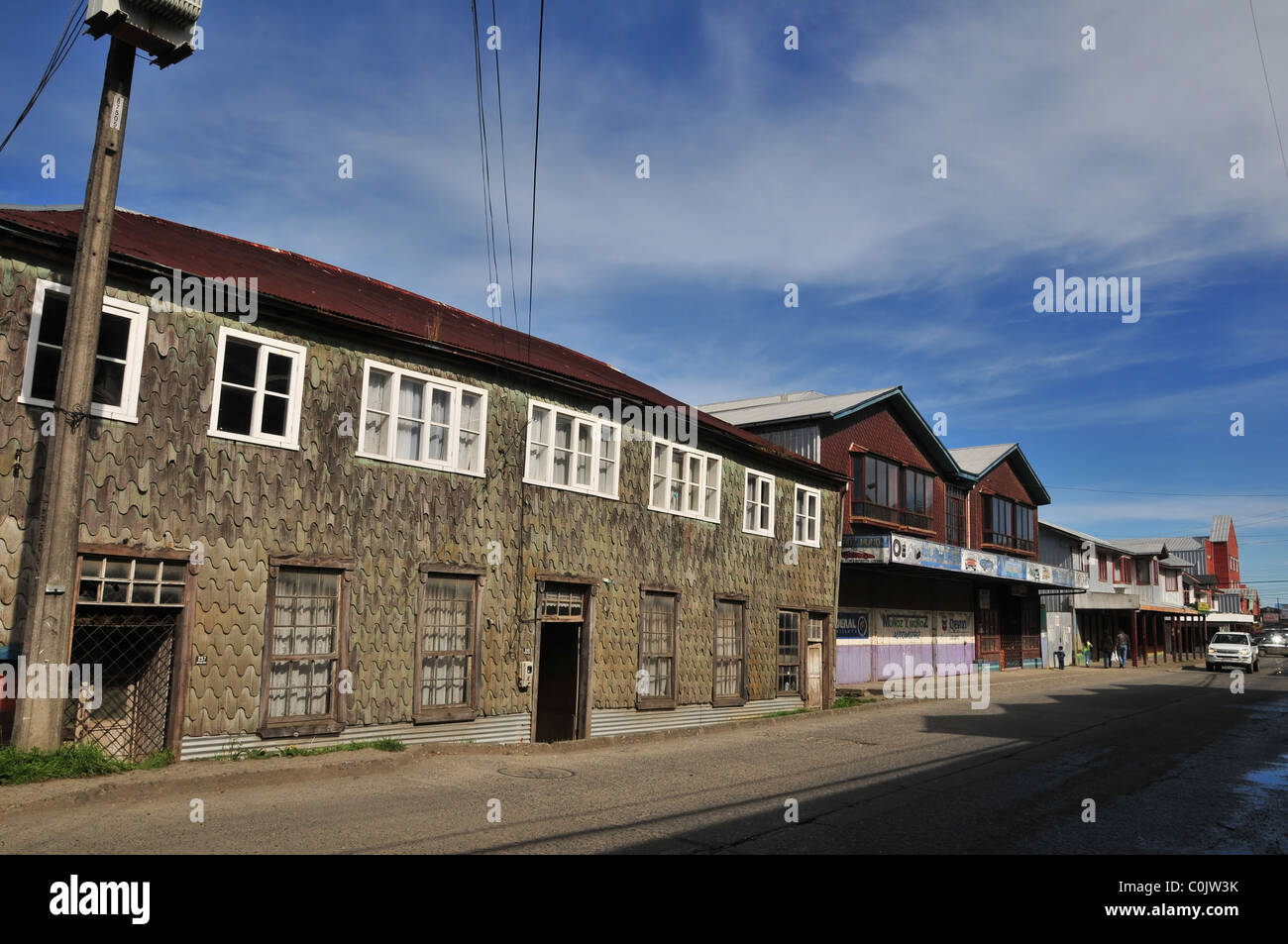 Blue sky urban street view di scandole in legno edifici, con lamiera ondulata di tetti, Arturo Prat, Ancud, Isola di Chiloe, Cile Foto Stock