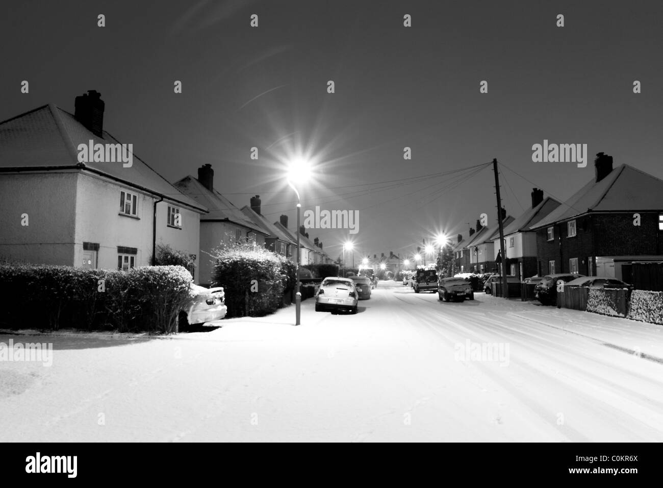 Una coperta di neve road con case illuminato da luci di strada al buio. Foto Stock