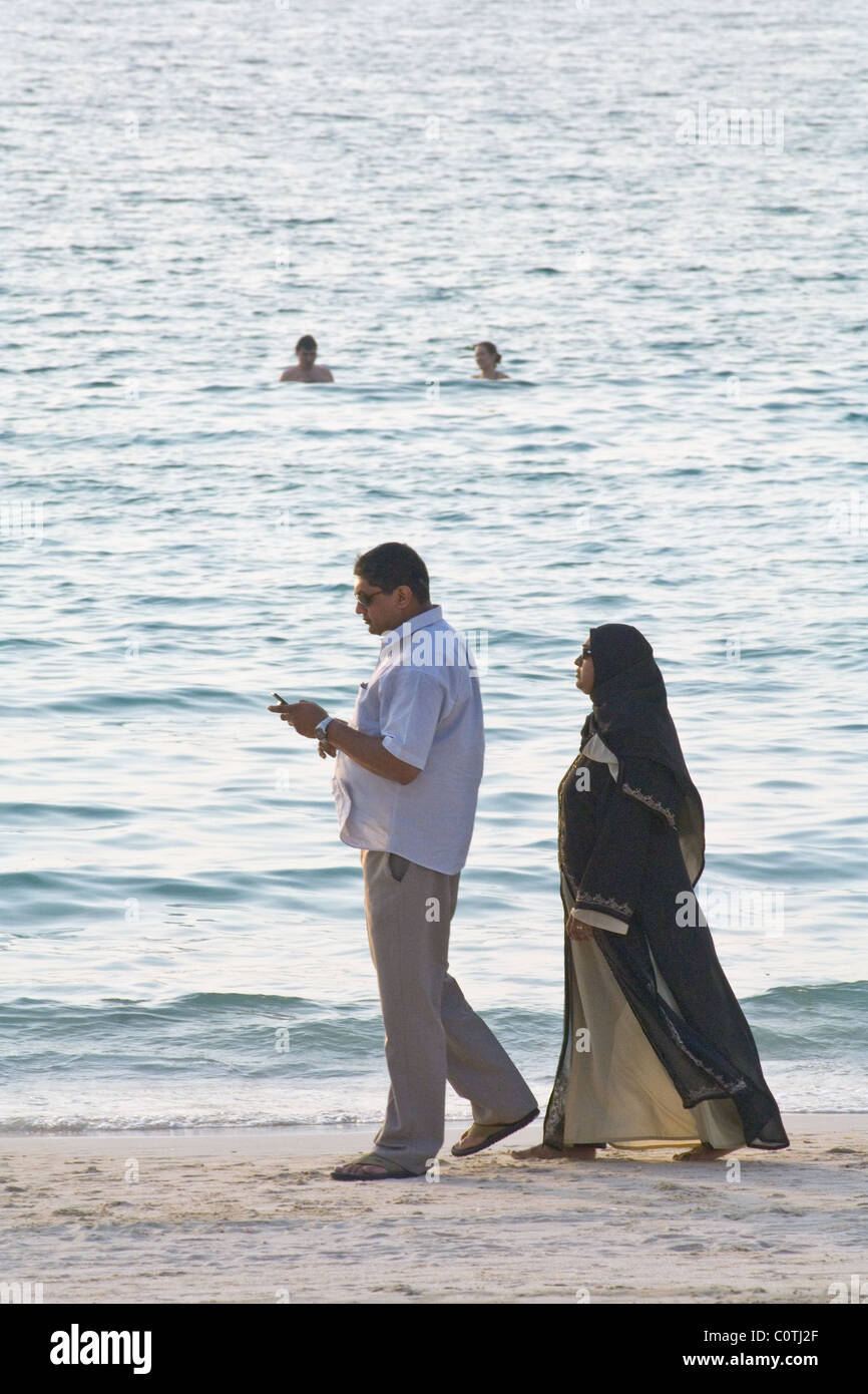 Uomo che utilizza un telefono cellulare mentre si cammina con una donna su una spiaggia di Dubai Foto Stock