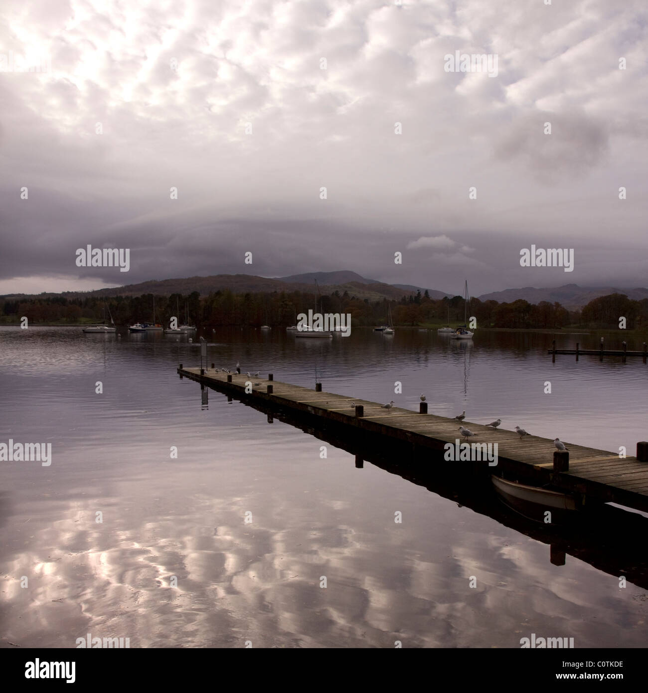 Cielo nuvoloso le riflessioni e il molo sul Lago di Windermere, Ambleside, Lake District, Cumbria, England, Regno Unito Foto Stock