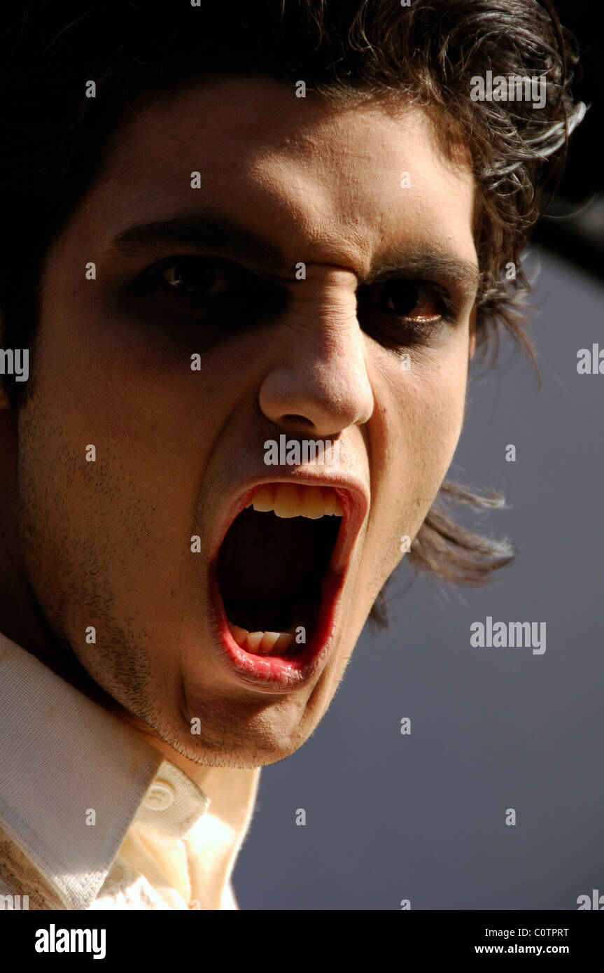 La faccia di un giovane uomo vestito come un vampiro o zombie con bocca aperta Foto Stock