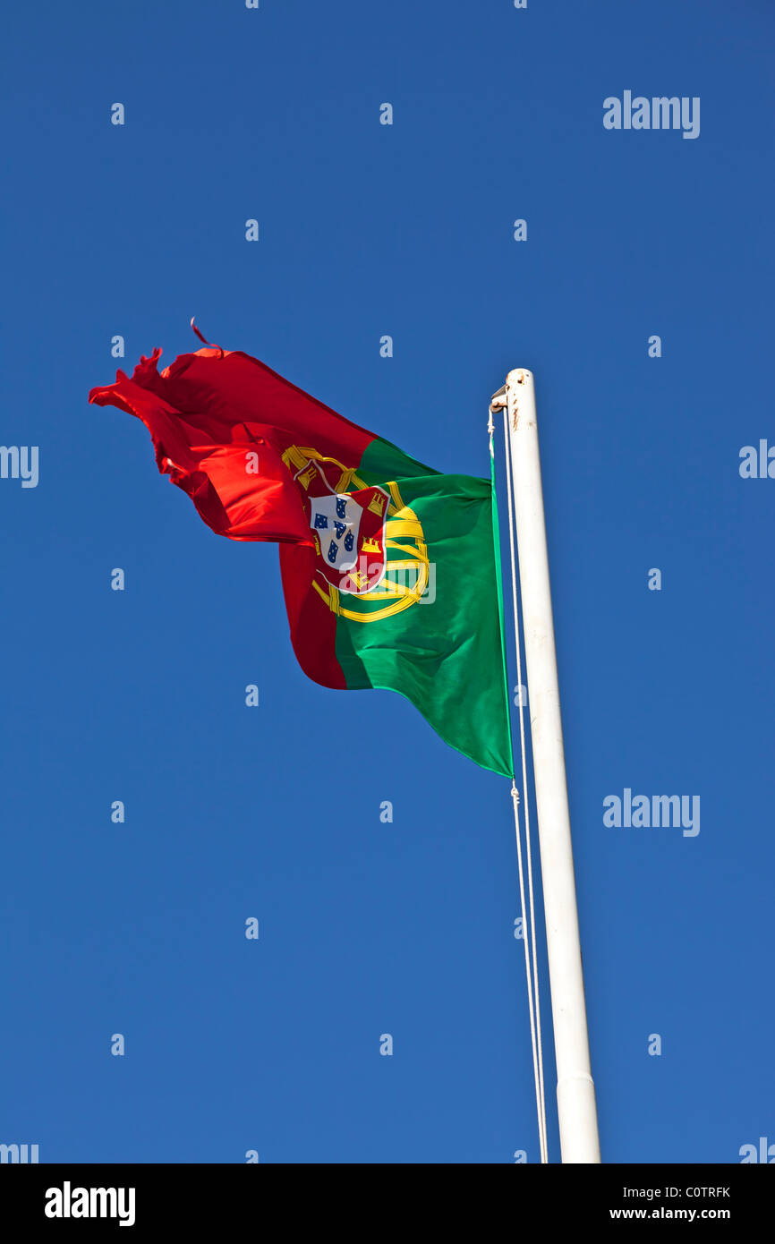 Bandiera portoghese sventolare su un palo con un chiaro blu cielo soleggiato in background Foto Stock