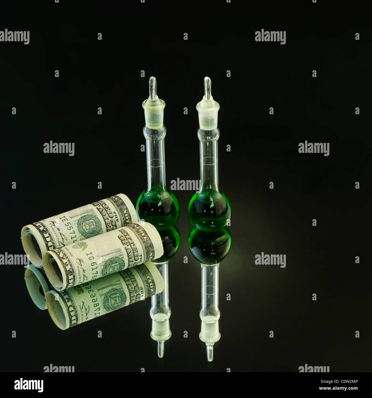 Due bicchieri di laboratorio con liquido verde accanto alla moneta americana su una base di specchio con luce flare sui bicchieri di verde. Foto Stock