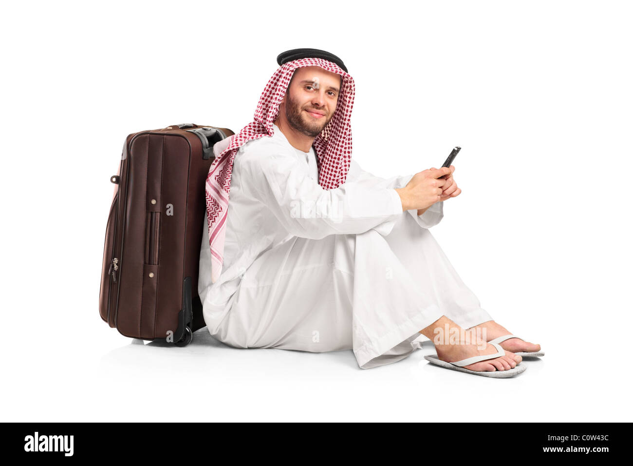 Uomo arabo seduta vicino una valigia e la digitazione di un messaggio di testo sul suo cellulare Foto Stock