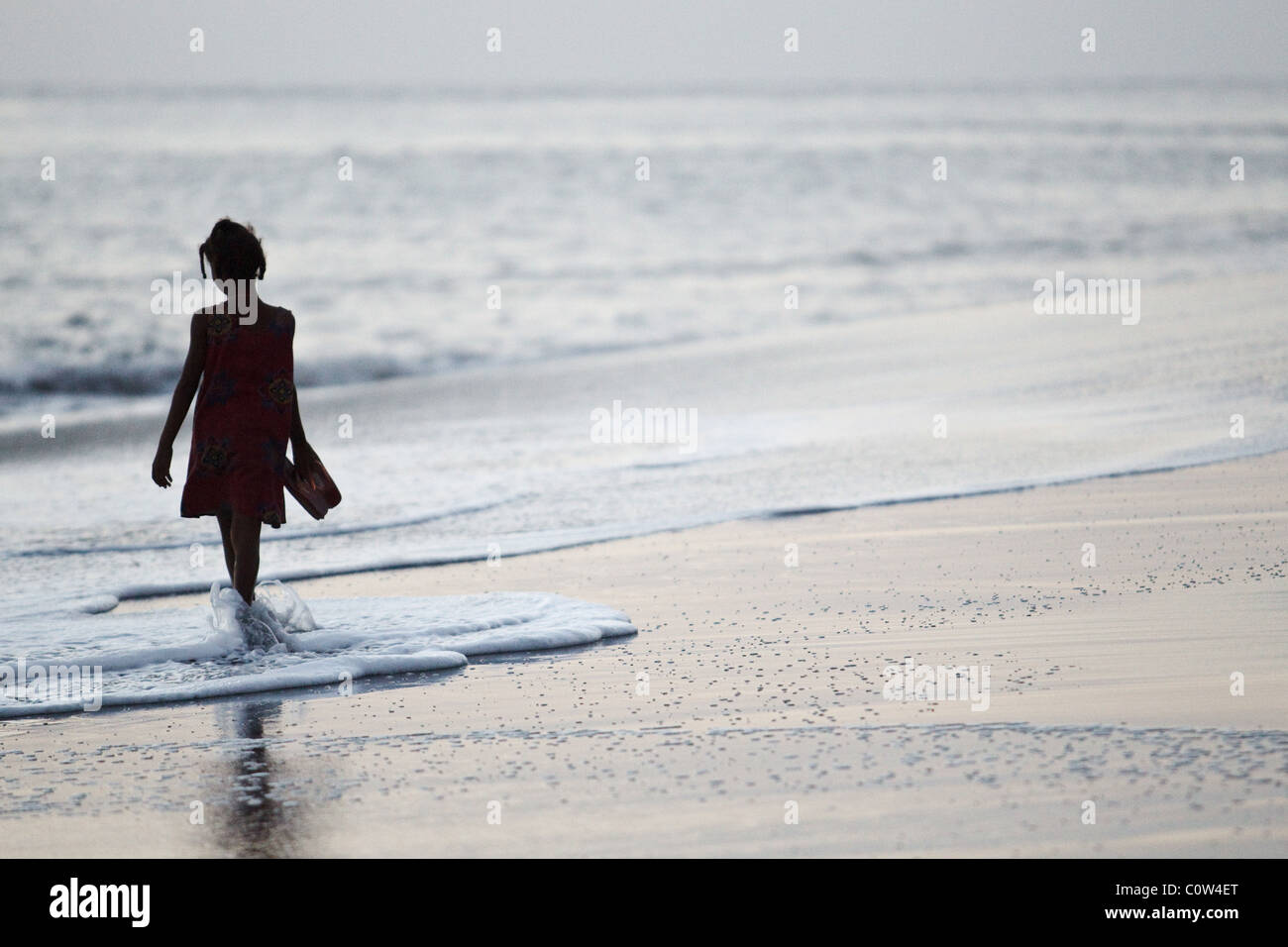 Una giovane ragazza con sandali in mano destra passeggiate sulla spiaggia al tramonto vicino a Sao Filipe, isola di Fogo, Capo Verde Foto Stock