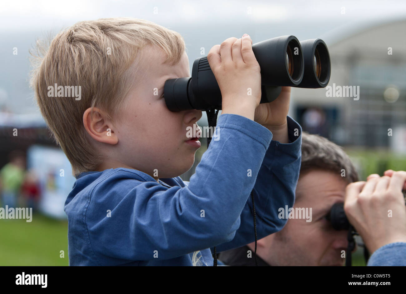 Ragazzo guardando gli aeroplani con un binocolo in corrispondenza di un'esibizione aerea Foto Stock