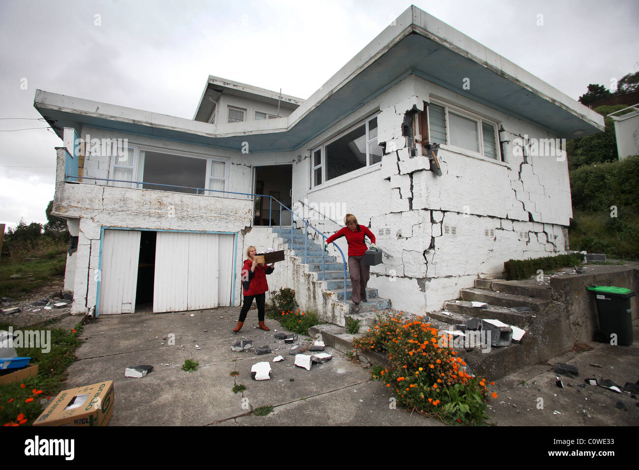 I residenti di fretta per rimuovere la proprietà da un male casa danneggiata in Sumner, Christchurch, seguendo il 6.3 terremoto di magnitudine. Foto Stock