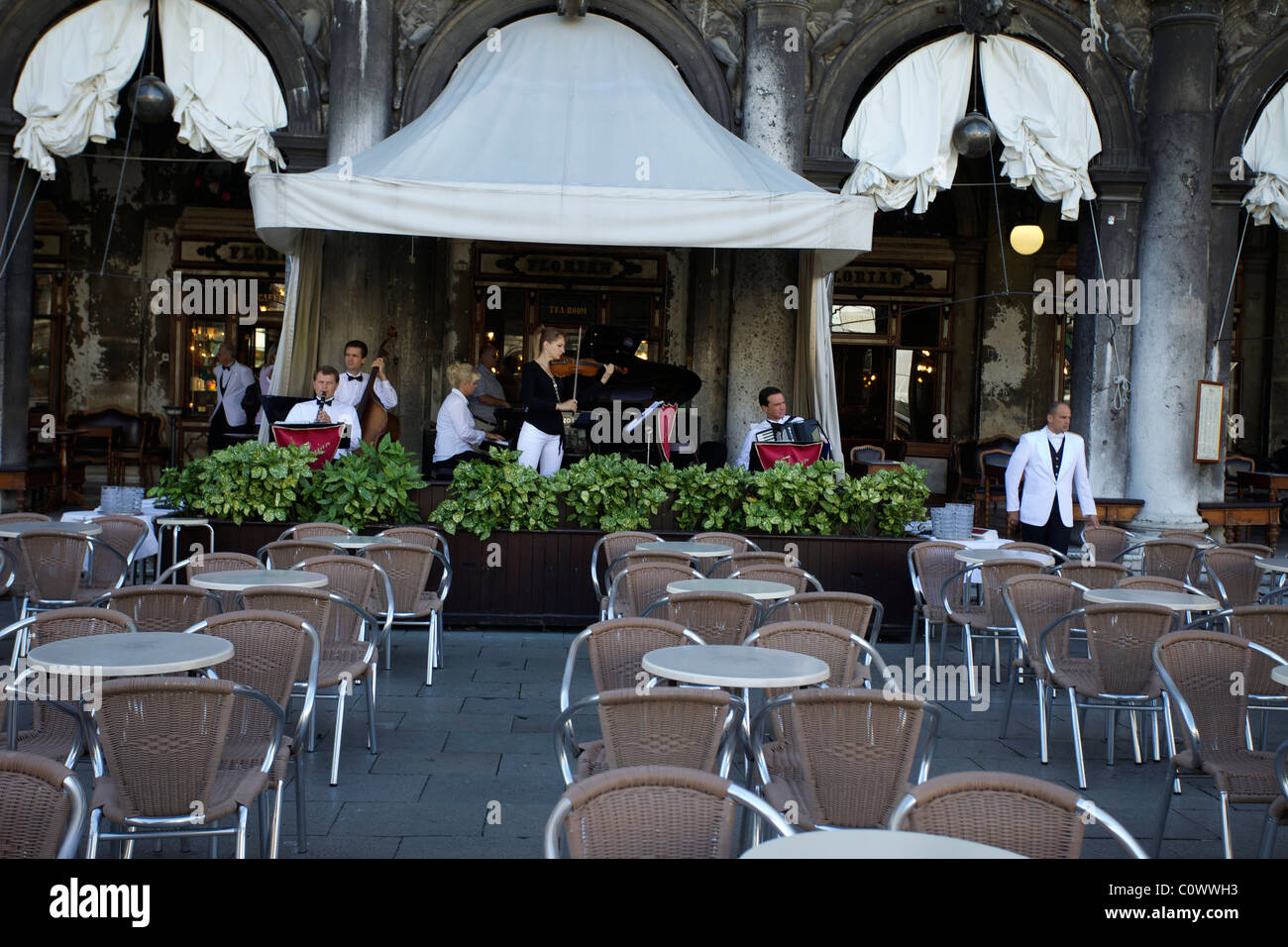 Una banda che suona presso uno dei ristoranti sulla piazza San Marco Piazza nel tentativo di vincere un affare. Tabelle vuote in primo piano. Foto Stock