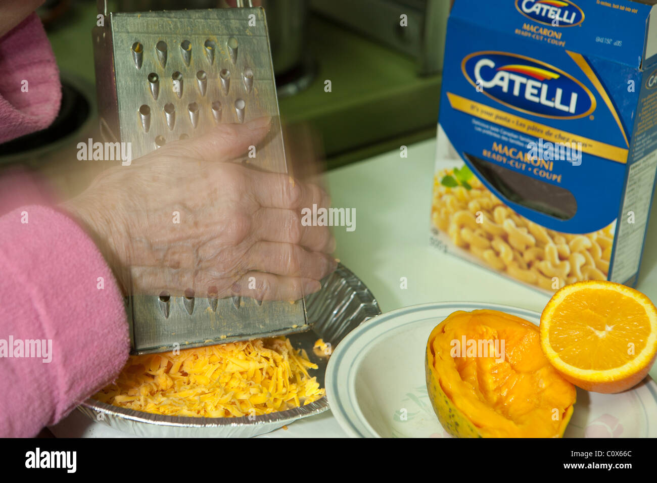 Signora anziana grattugiare il formaggio per maccheroni cena-Victoria, British Columbia, Canada. Foto Stock