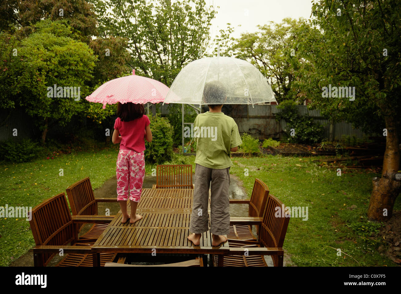 Un ragazzo e una ragazza, di stare in piedi sulla tavola in giardino e ammirare la pioggia in un fine settimana. Foto Stock