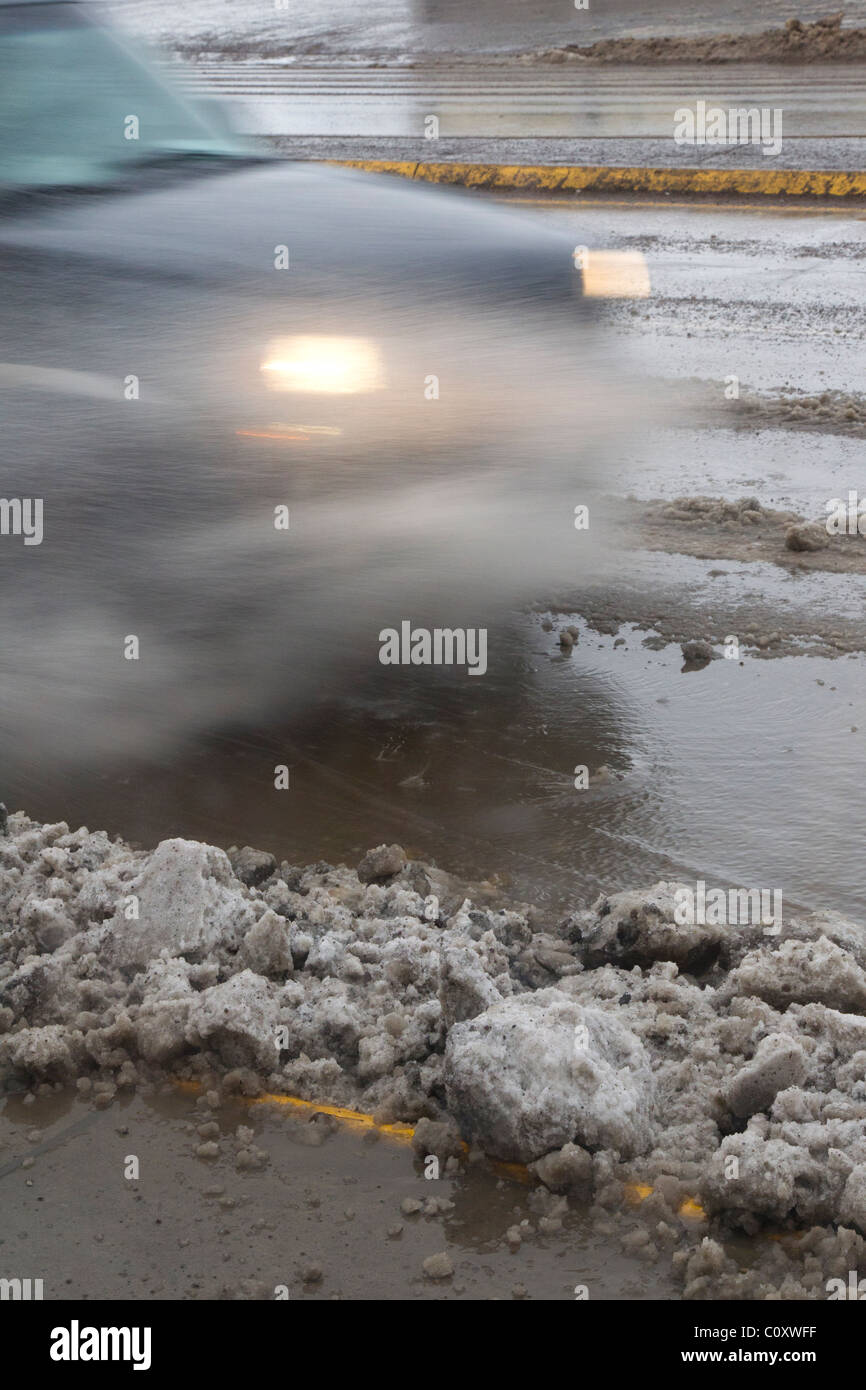 Slush vola come unità di traffico su una neve e neve melt coperto sezione di strada. Foto Stock