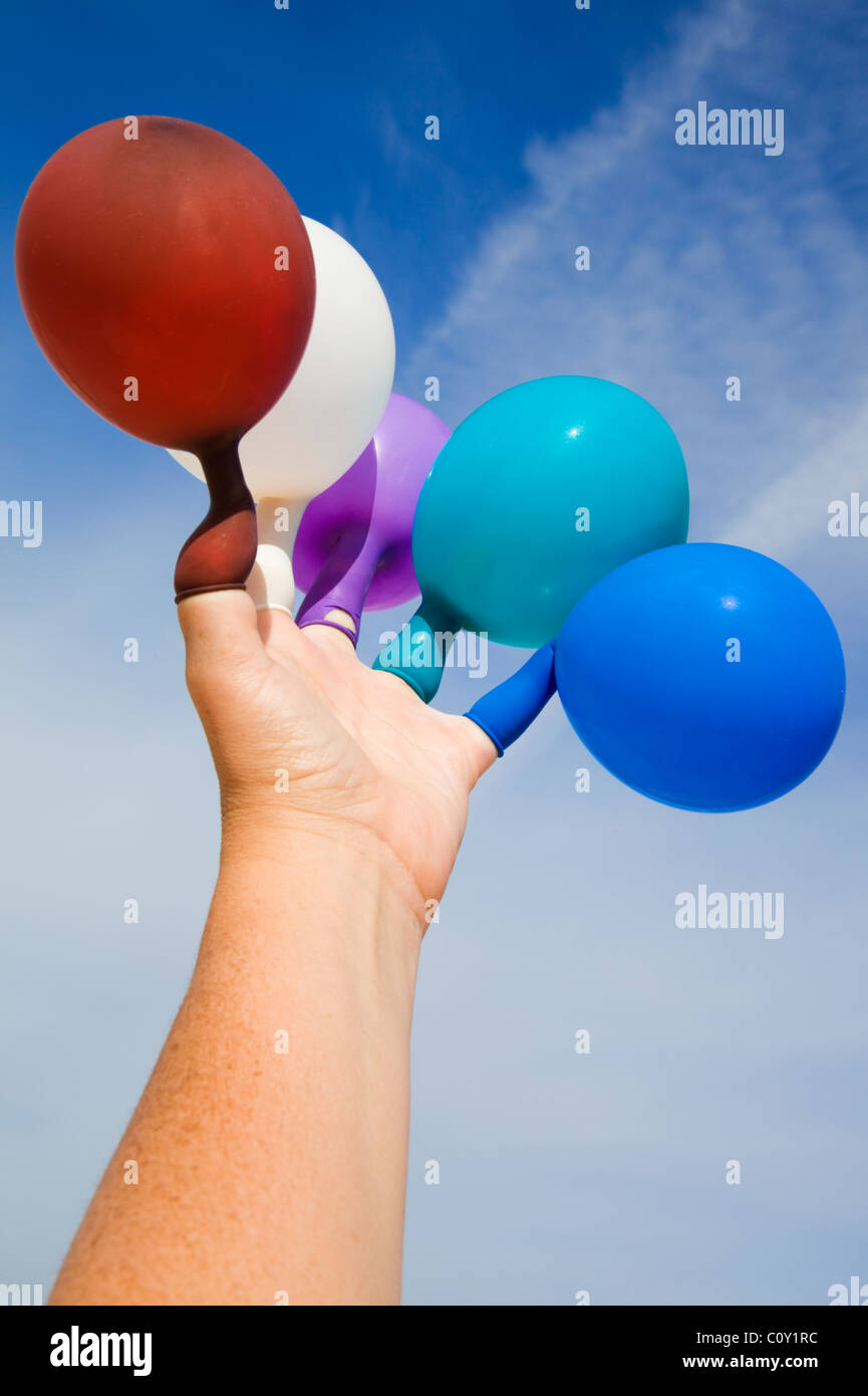 Mano con palloncini colorati sulle dita contro un nuvoloso cielo blu Foto Stock