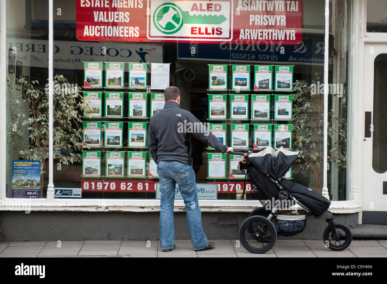 Un giovane padre spingendo un buggy guardando la casa prezzi in un agenti immobiliari finestra REGNO UNITO Foto Stock