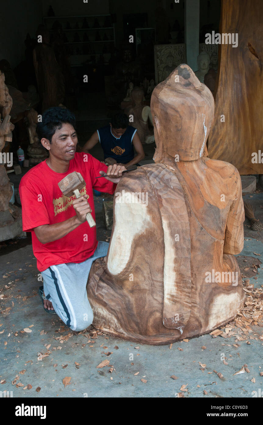 Un Balinese artigiano scultore in legno a lavorare su una scultura di un grande Buddha seduto nel villaggio di Peliatan Foto Stock